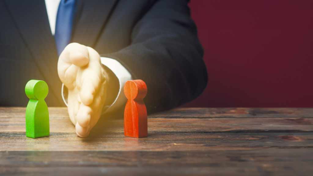 A man putting his hand between two toy people, symbolizing conflict resolution